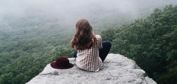 A girl sitting on top of a mountain on a flat rock. Gazing out over the valley.